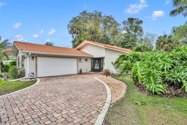 view of front of house featuring a tiled roof, decorative driveway, a garage, and stucco siding