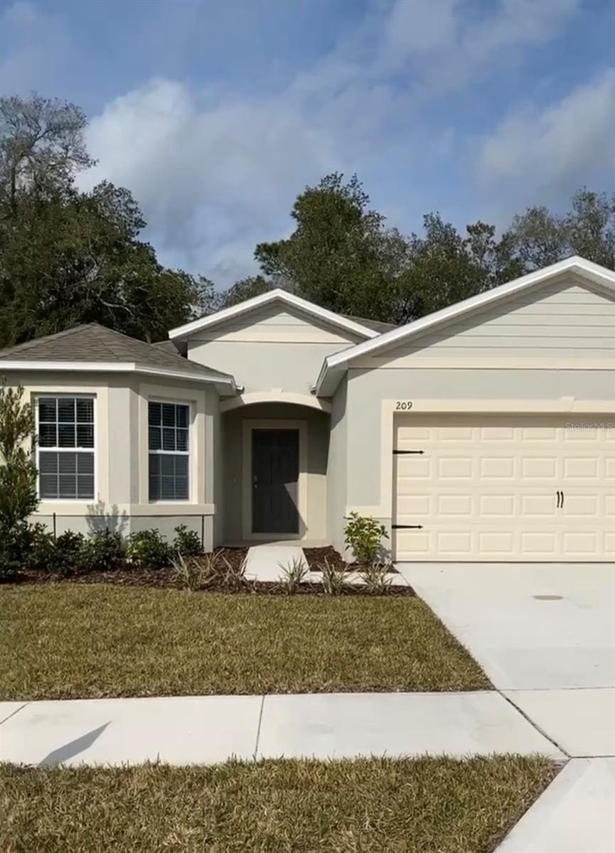 single story home with concrete driveway, a front yard, an attached garage, and stucco siding