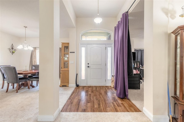 entrance foyer with carpet floors, a chandelier, baseboards, and wood finished floors