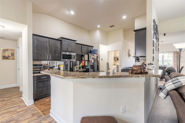 kitchen with visible vents, stainless steel microwave, black refrigerator with ice dispenser, light wood-style flooring, and a towering ceiling