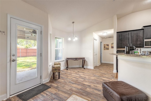 interior space featuring baseboards, stainless steel microwave, wood finished floors, vaulted ceiling, and a notable chandelier