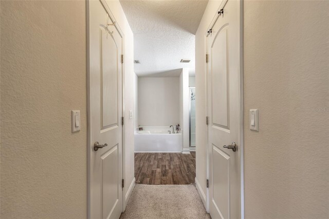 hall featuring a textured ceiling, a textured wall, wood finished floors, and visible vents