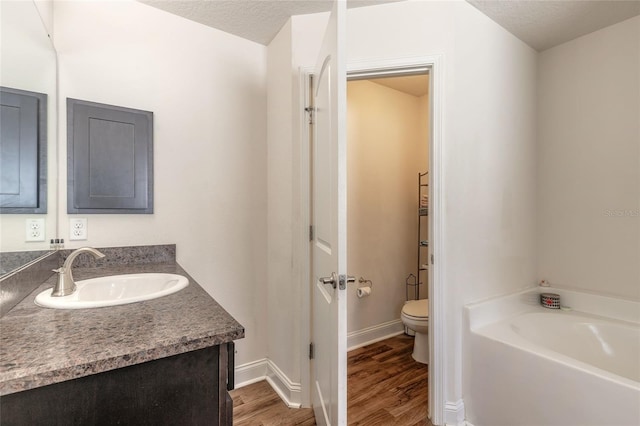 full bath with toilet, wood finished floors, a garden tub, a textured ceiling, and vanity