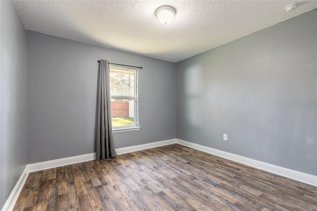 empty room with dark wood-style floors, a textured ceiling, and baseboards