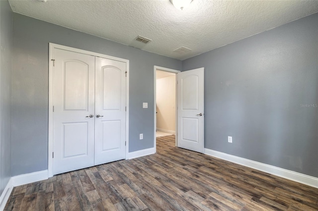 unfurnished bedroom featuring a textured ceiling, visible vents, baseboards, a closet, and dark wood-style floors