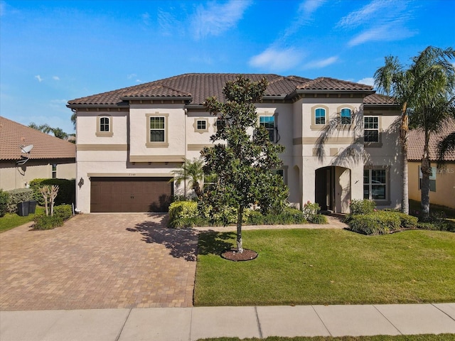 mediterranean / spanish house featuring an attached garage, a tile roof, decorative driveway, stucco siding, and a front lawn