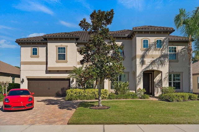 mediterranean / spanish-style house with decorative driveway, a tile roof, a front lawn, and stucco siding