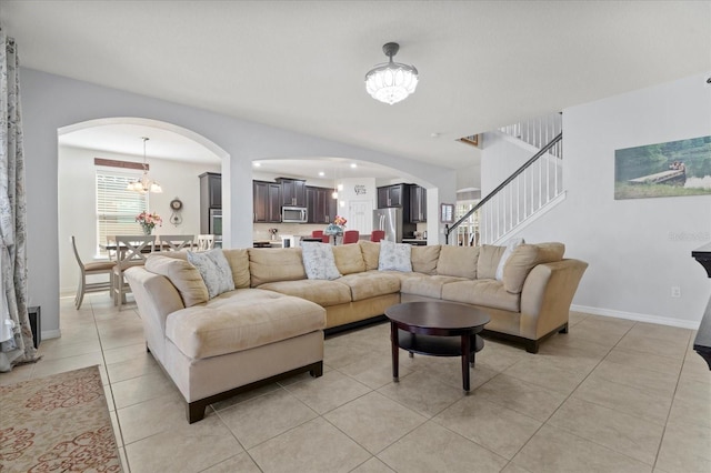 living room with a chandelier, light tile patterned floors, arched walkways, baseboards, and stairway