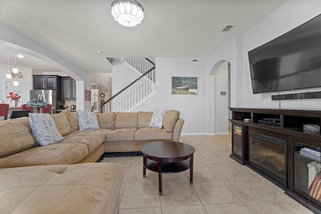 living area with stairs, arched walkways, baseboards, and light tile patterned floors