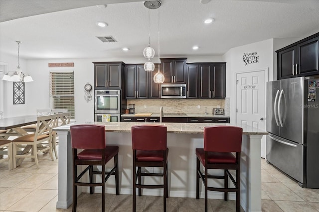 kitchen featuring an island with sink, light tile patterned floors, appliances with stainless steel finishes, and backsplash