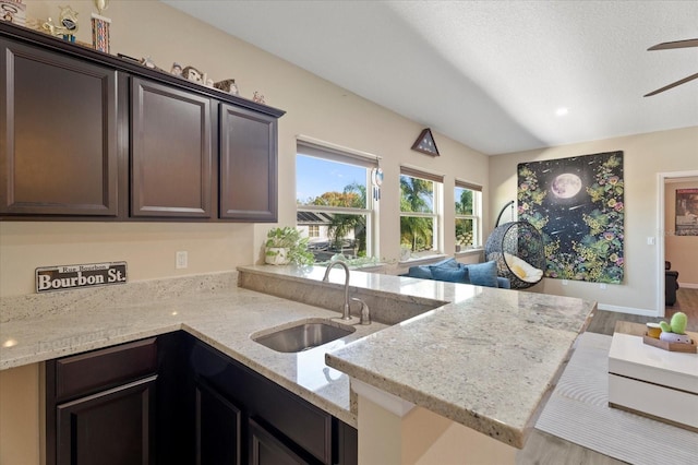 kitchen featuring ceiling fan, light stone counters, a peninsula, dark brown cabinets, and a sink