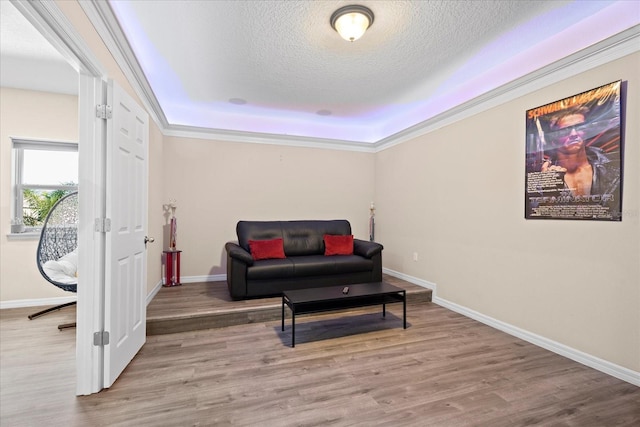 living area featuring a textured ceiling, wood finished floors, baseboards, ornamental molding, and a raised ceiling