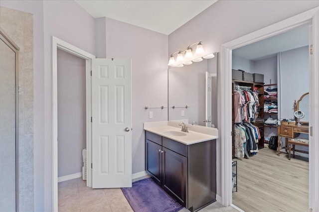 full bathroom featuring a walk in closet, vanity, baseboards, and tile patterned floors