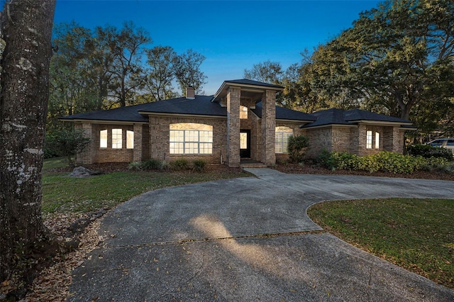 prairie-style house with driveway, brick siding, a chimney, and a front yard