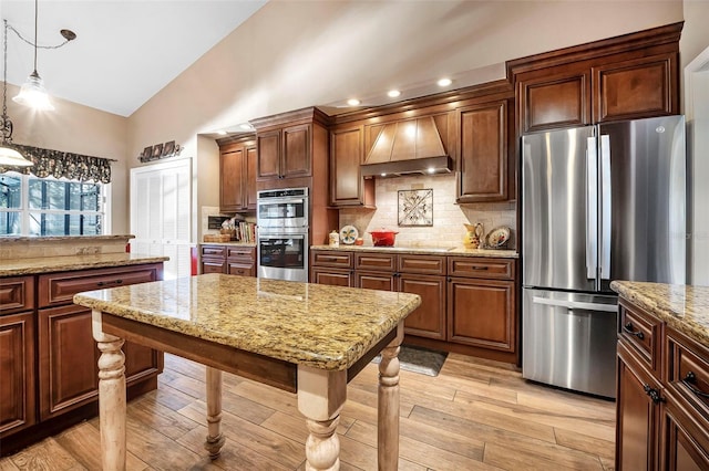 kitchen featuring light wood-style flooring, appliances with stainless steel finishes, decorative light fixtures, vaulted ceiling, and premium range hood