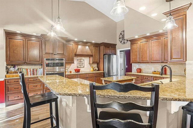 kitchen featuring custom range hood, appliances with stainless steel finishes, a breakfast bar area, a peninsula, and light stone countertops