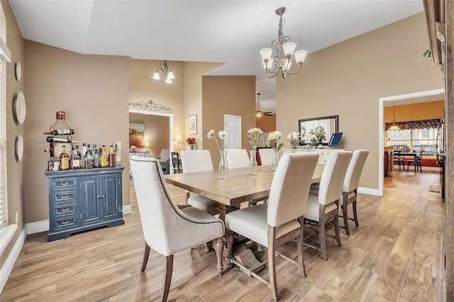 dining area with high vaulted ceiling, a notable chandelier, light wood-style flooring, and baseboards