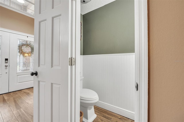 bathroom with a wainscoted wall, toilet, and wood finished floors