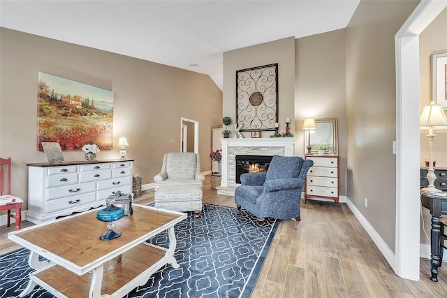 sitting room featuring baseboards, vaulted ceiling, wood finished floors, and a stone fireplace