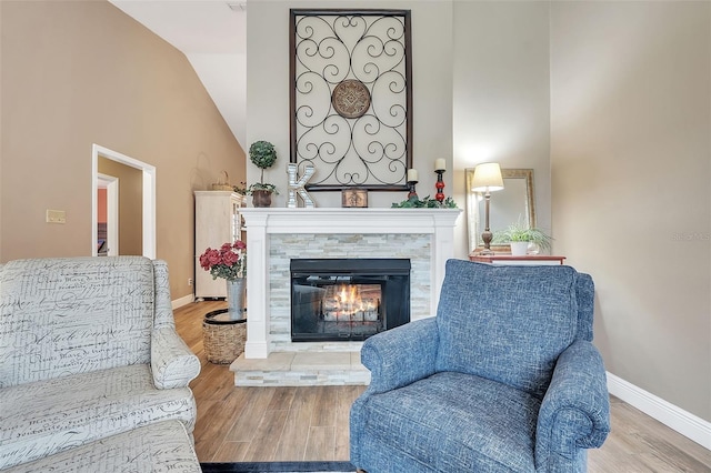 living area with high vaulted ceiling, a glass covered fireplace, baseboards, and wood finished floors