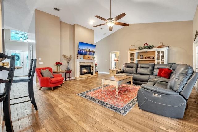 living area with high vaulted ceiling, visible vents, a fireplace, and wood finished floors