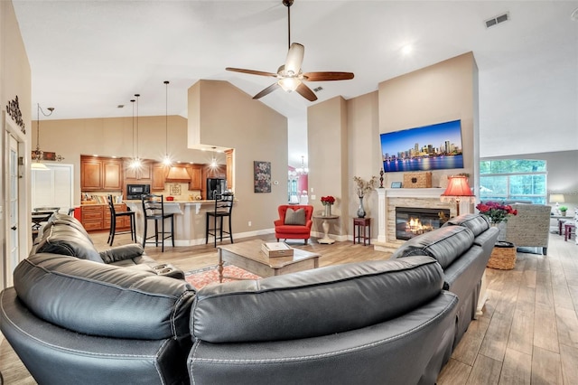 living area featuring ceiling fan, high vaulted ceiling, a stone fireplace, visible vents, and light wood-style floors