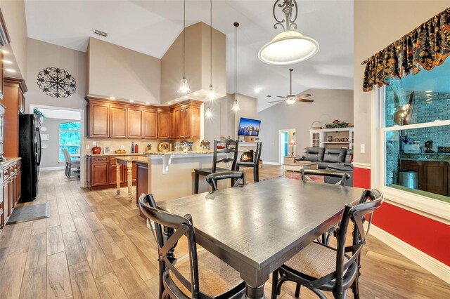 dining space featuring a ceiling fan, baseboards, high vaulted ceiling, and light wood finished floors