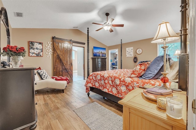 bedroom featuring lofted ceiling, ceiling fan, a barn door, light wood-style flooring, and visible vents