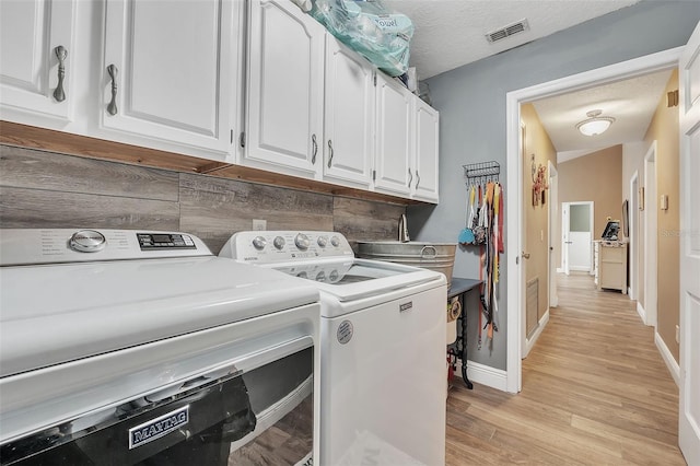 clothes washing area featuring visible vents, cabinet space, light wood-style flooring, and washing machine and clothes dryer