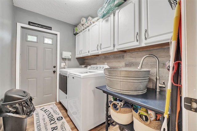 clothes washing area featuring a textured ceiling, light wood-type flooring, independent washer and dryer, and cabinet space