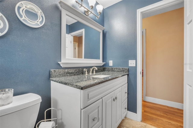 half bath featuring toilet, vanity, baseboards, and wood finished floors