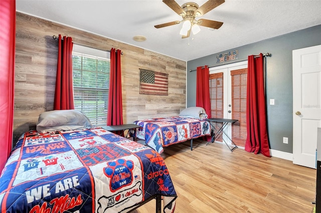 bedroom featuring french doors, ceiling fan, wooden walls, wood finished floors, and baseboards