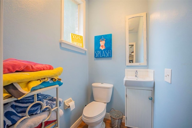 half bath with toilet, vanity, baseboards, and wood finished floors