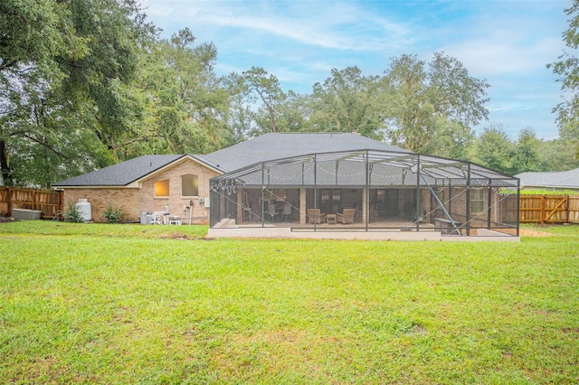 back of property featuring glass enclosure, a lawn, and fence