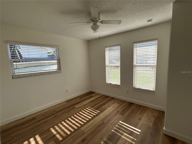 spare room featuring a healthy amount of sunlight, a textured ceiling, baseboards, and wood finished floors