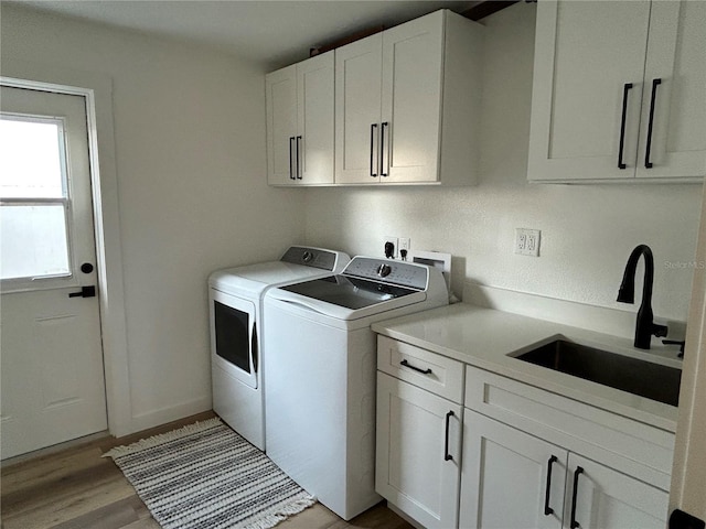 laundry area featuring independent washer and dryer, a sink, cabinet space, and light wood-style floors