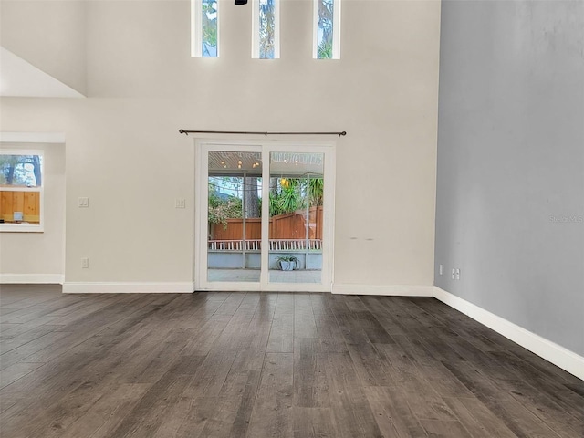 unfurnished living room with dark wood-style floors, baseboards, and a towering ceiling