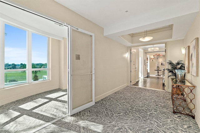 hall featuring carpet, baseboards, and a raised ceiling