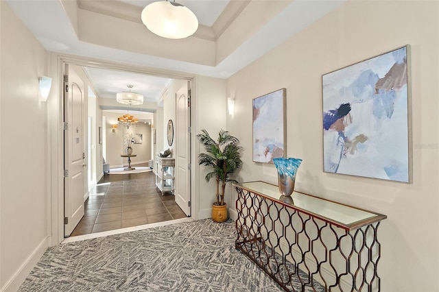 hallway featuring crown molding, carpet flooring, baseboards, a raised ceiling, and an inviting chandelier