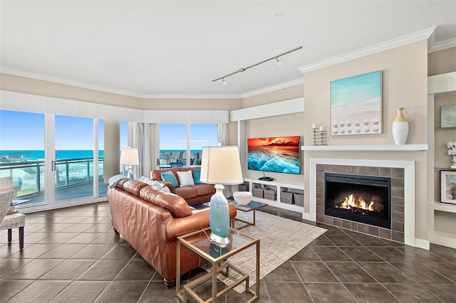 tiled living area featuring a water view, rail lighting, crown molding, and a tile fireplace