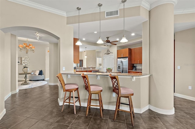 kitchen with brown cabinetry, visible vents, stainless steel refrigerator with ice dispenser, and a kitchen breakfast bar