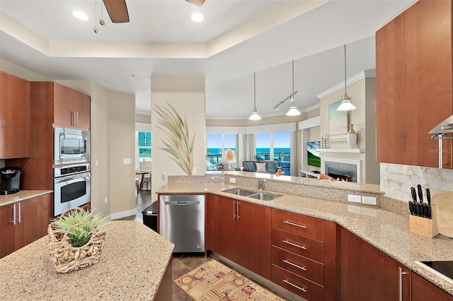 kitchen with light stone counters, a sink, appliances with stainless steel finishes, brown cabinets, and decorative light fixtures