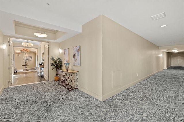 hallway featuring baseboards, visible vents, a raised ceiling, and carpet flooring