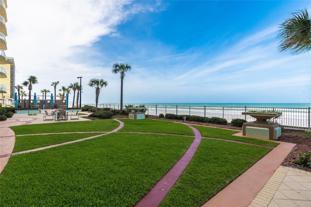 view of property's community featuring a yard, a beach view, a water view, a patio area, and fence