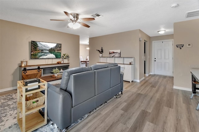 living area with visible vents, light wood-style flooring, baseboards, and a textured ceiling