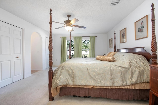 carpeted bedroom featuring arched walkways, ceiling fan, a textured ceiling, and visible vents