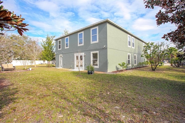 back of property with stucco siding, fence, and a yard