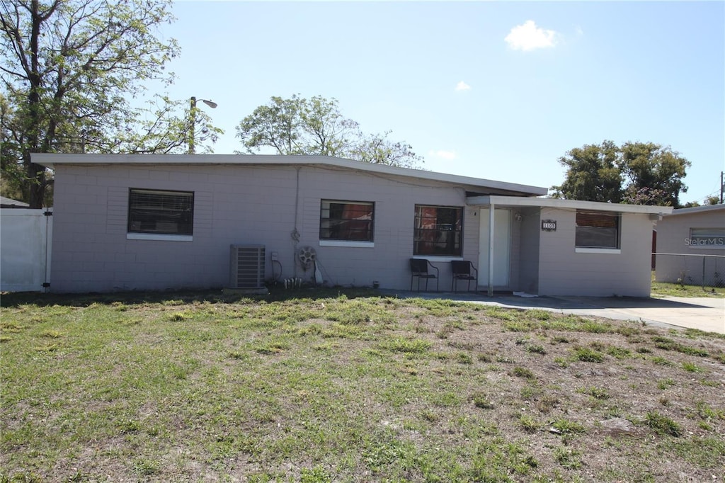 ranch-style house with cooling unit, concrete block siding, fence, and a front lawn