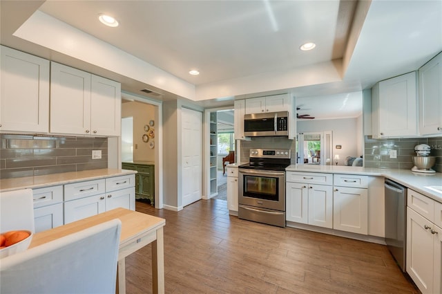 kitchen with light wood-style flooring, white cabinetry, light countertops, appliances with stainless steel finishes, and a tray ceiling