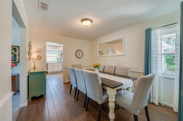 dining space with dark wood-style floors, baseboards, visible vents, and a textured ceiling